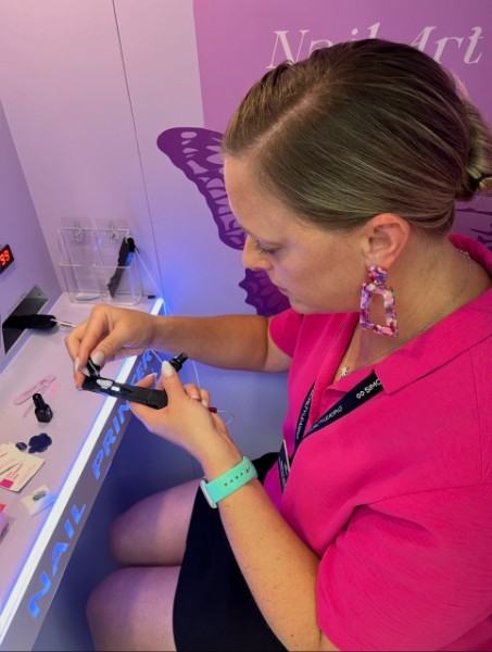 A woman working with nail-art tools at the workstation inside the lavender DIY booth.
