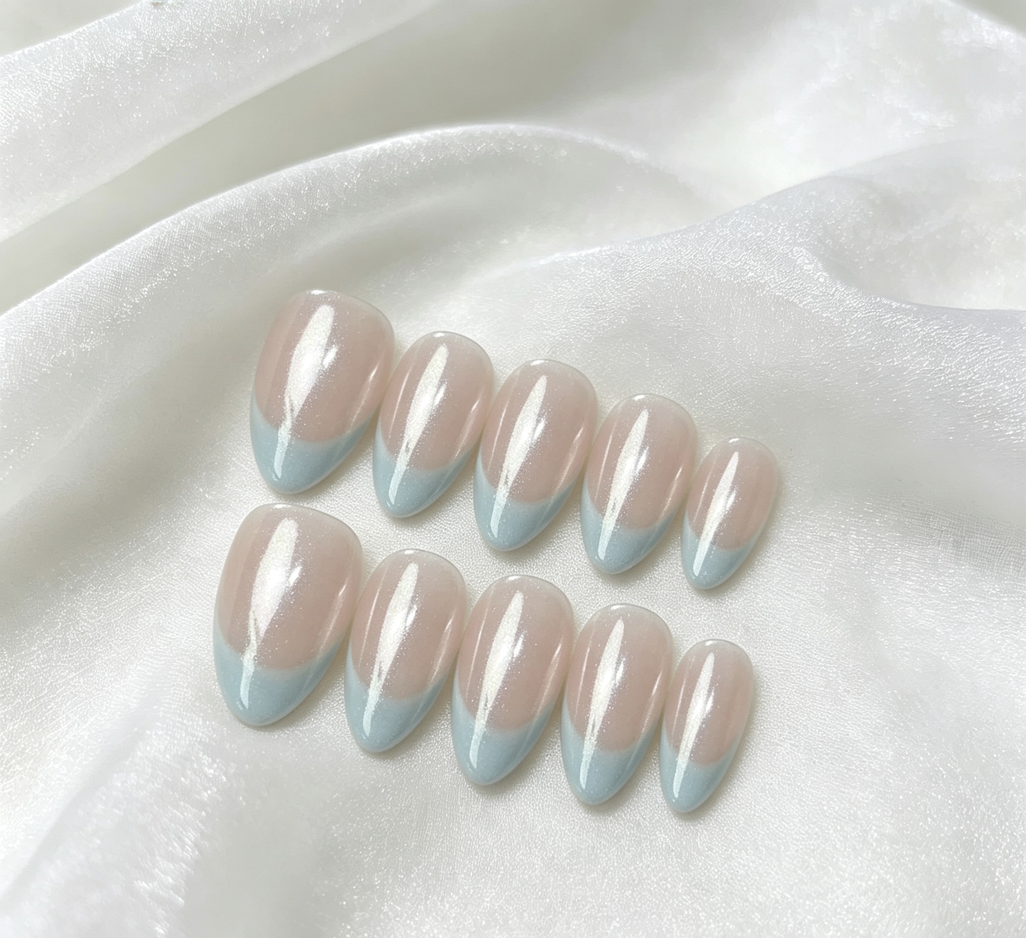 Glossy press-on nails with soft blue tips arranged on white fabric.