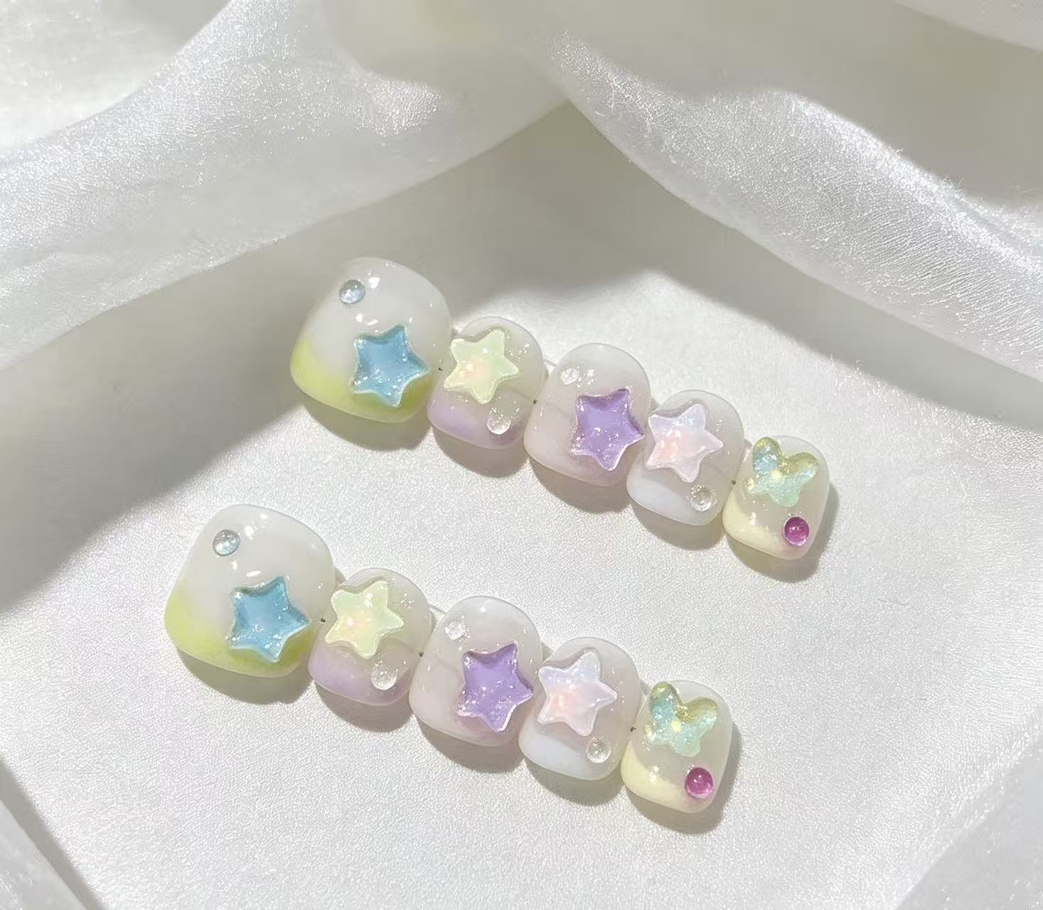 Short press-on nails decorated with pastel blue, yellow, purple and pink stars.