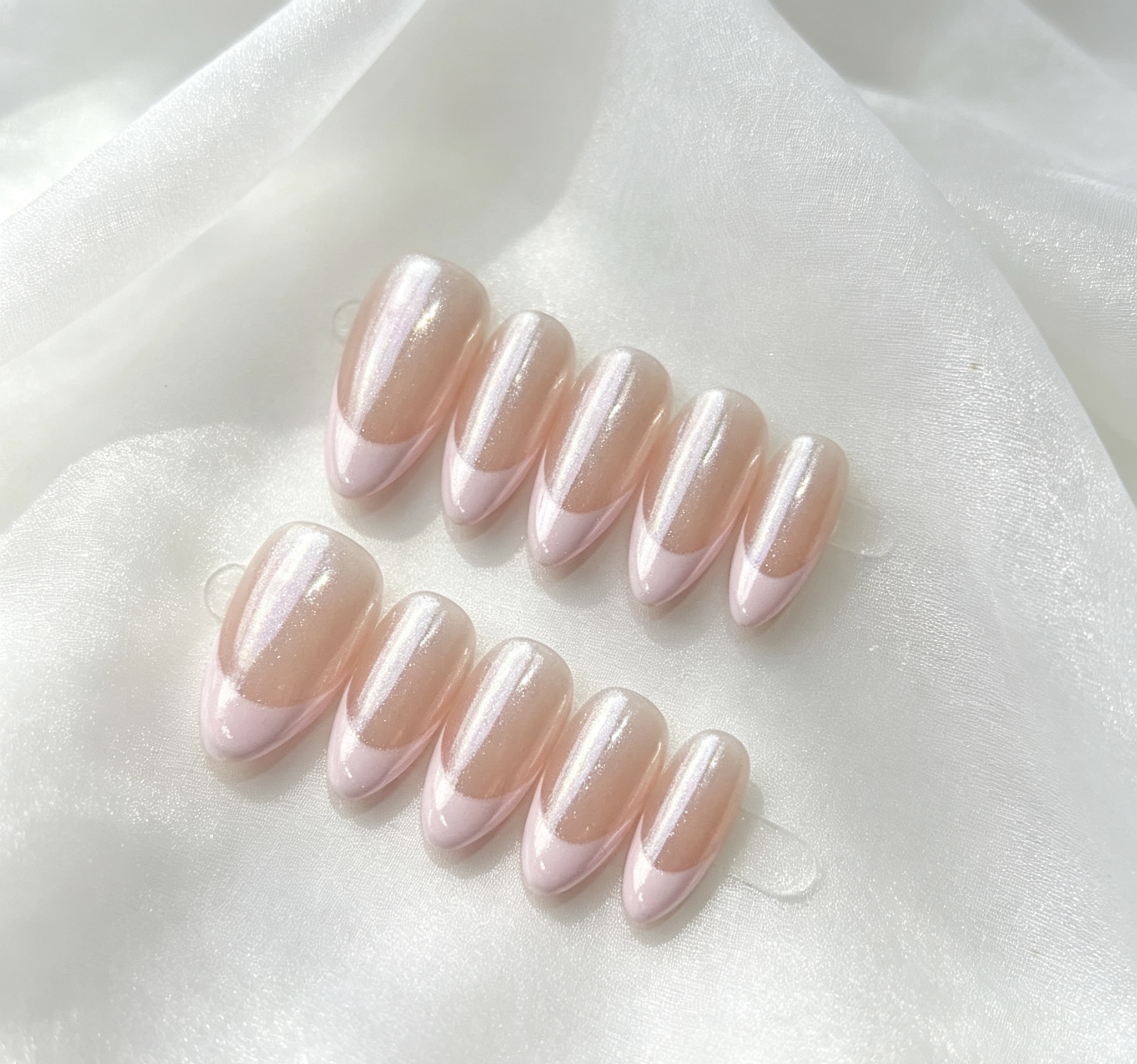 Two rows of almond-shaped pink press-on nails with a glossy sheen on white fabric.