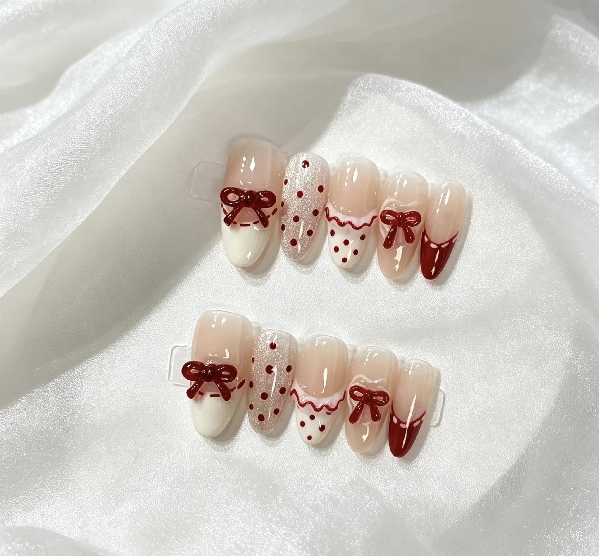 Press-on nails with red bows, dots and red-and-white tip designs on white fabric.