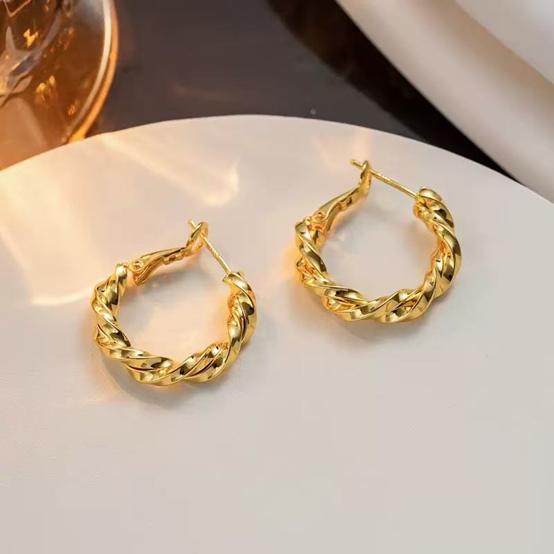 A pair of gold-tone hoop earrings with a twisted texture on a light-colored display.